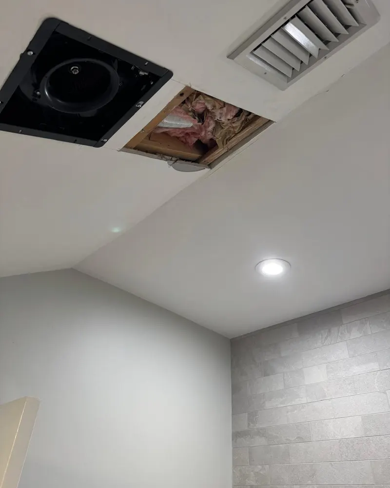 Bathroom ceiling opened next to the exhaust fan, showing framing and insulation